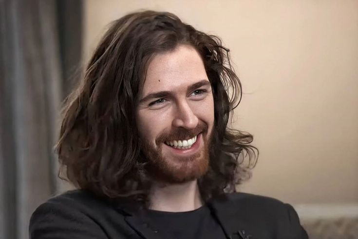 Hozier looking off camera smiling.
